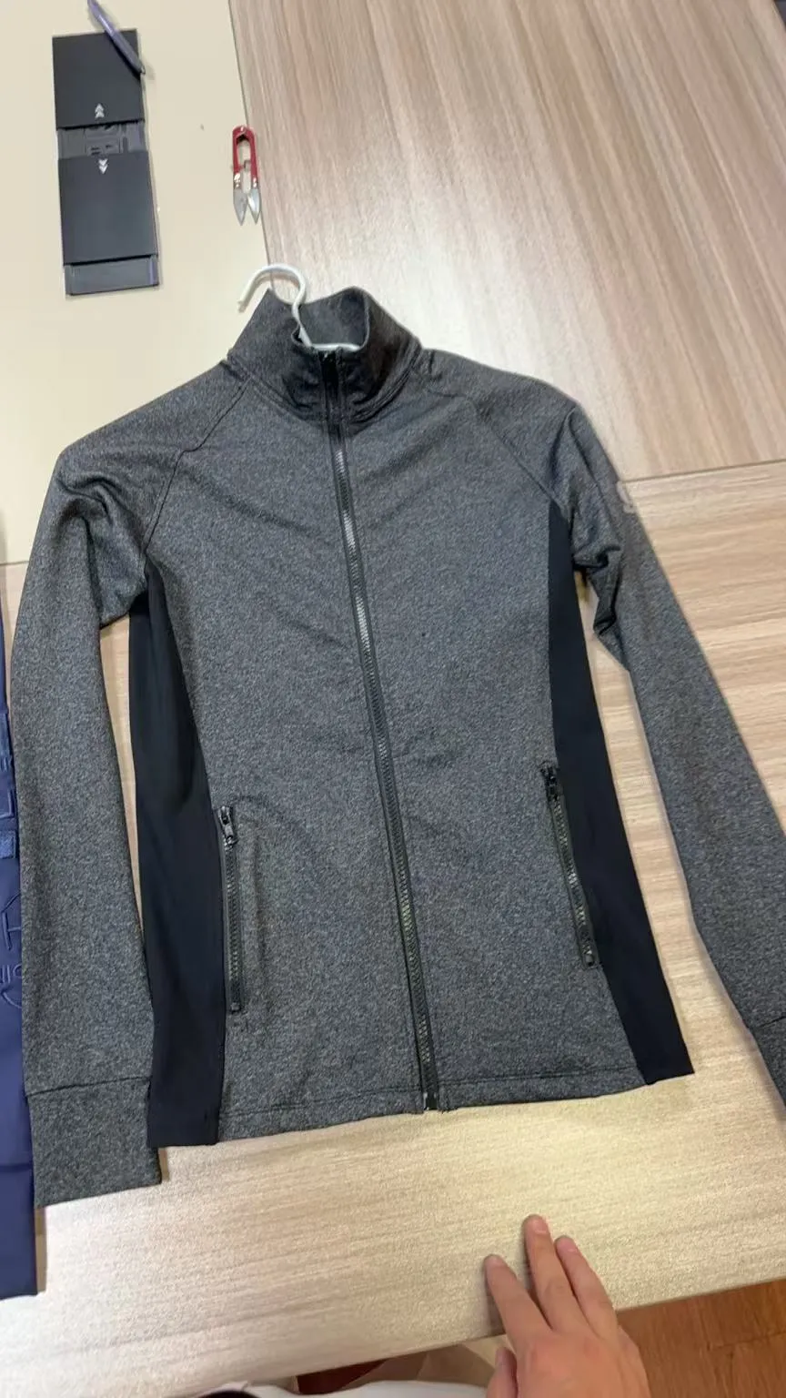 Grau melierte Trainingsjacke mit durchgehendem Reißverschluss und dunklen Seiteneinsätzen auf dem Bügel
